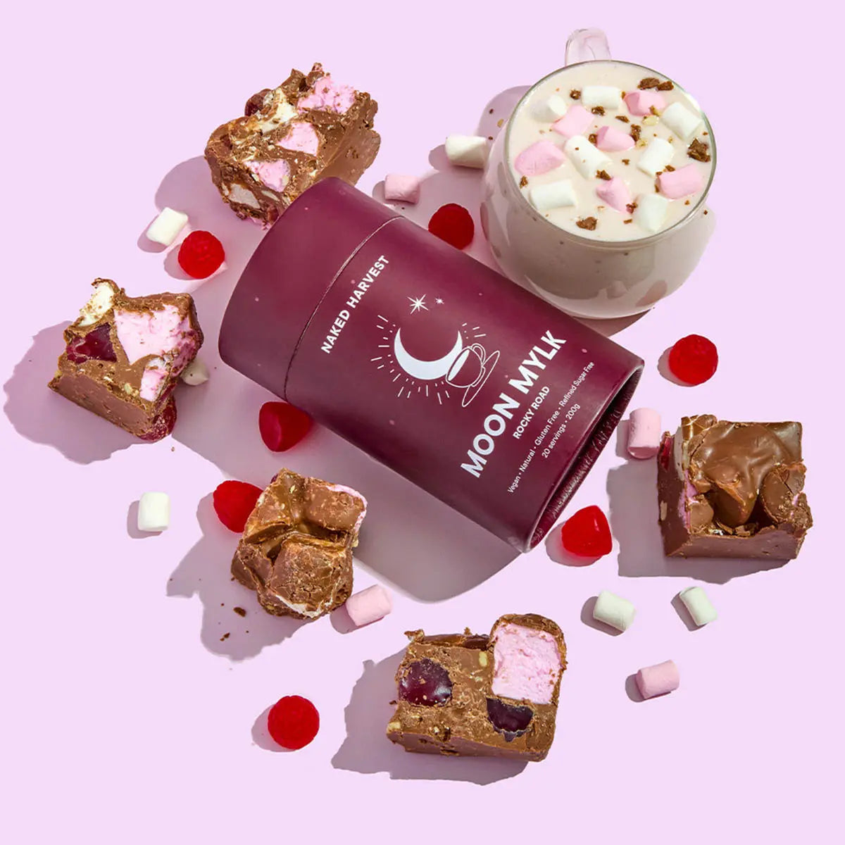 Cup of hot chocolate with marshmallows, rocky road squares, and a container labeled 'Moon Mylk' on a pink background.