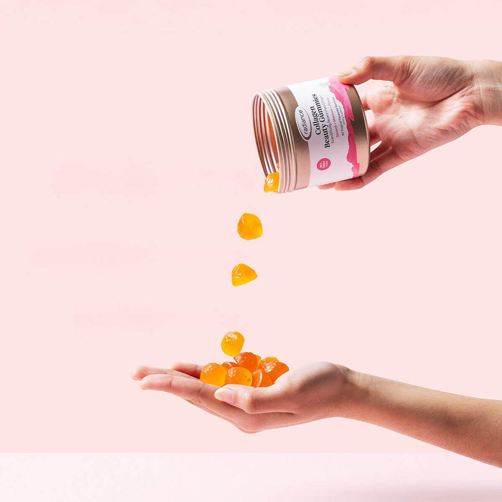 Hand holding a container of gummy vitamins with a pink background.