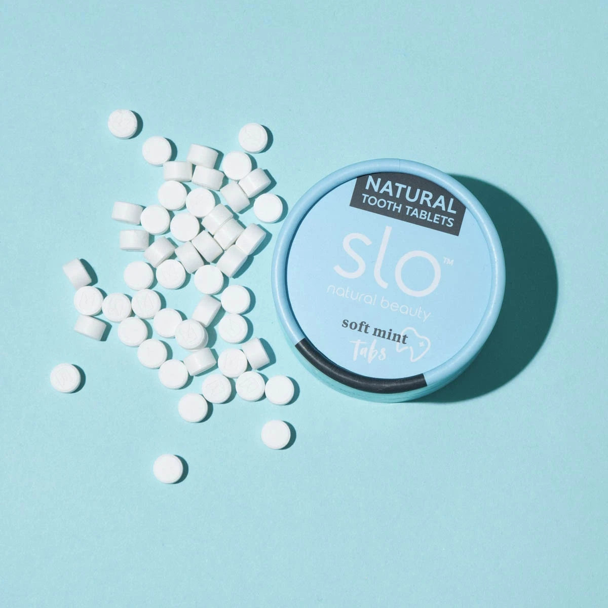Slo Tooth Tablets styled on a blue background with some tablets in a pile next to the packaging.