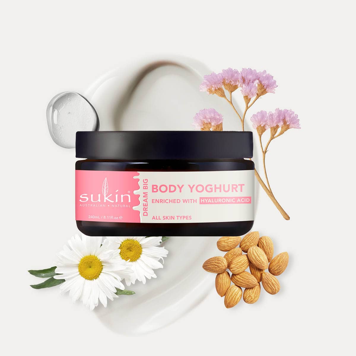 Sukin Body Yoghurt jar with flowers and almonds on a white background.