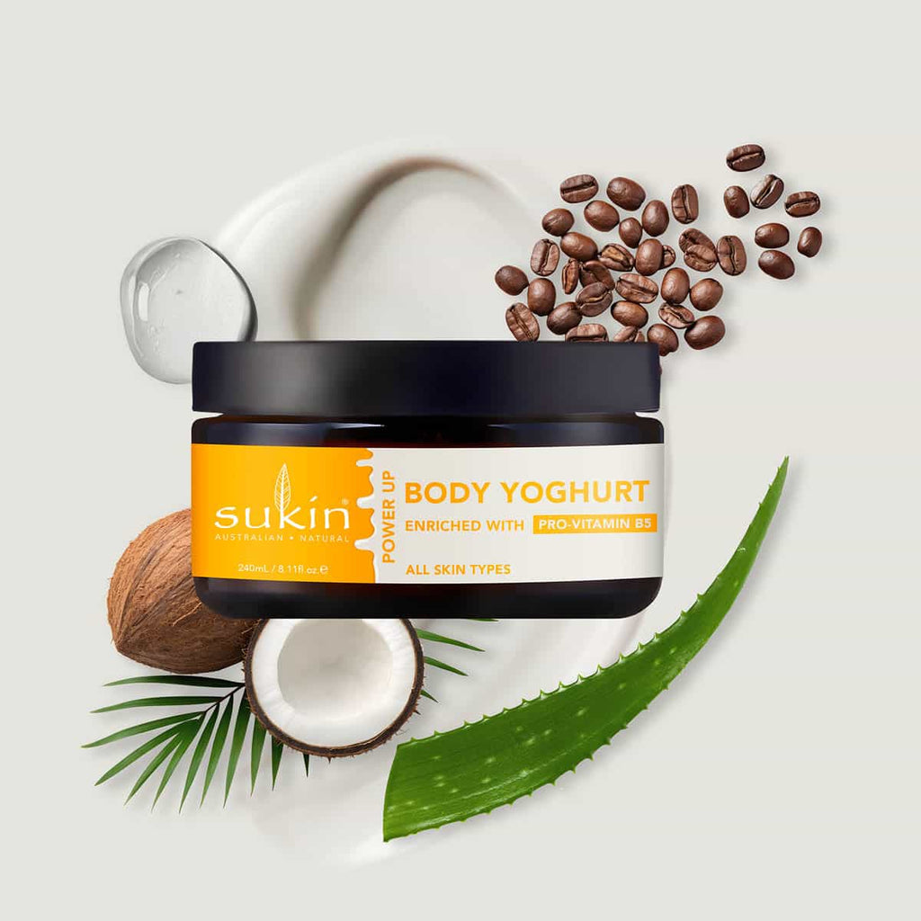Sukin Body Yoghurt jar with coffee beans, coconut, and aloe vera leaf on a light background.