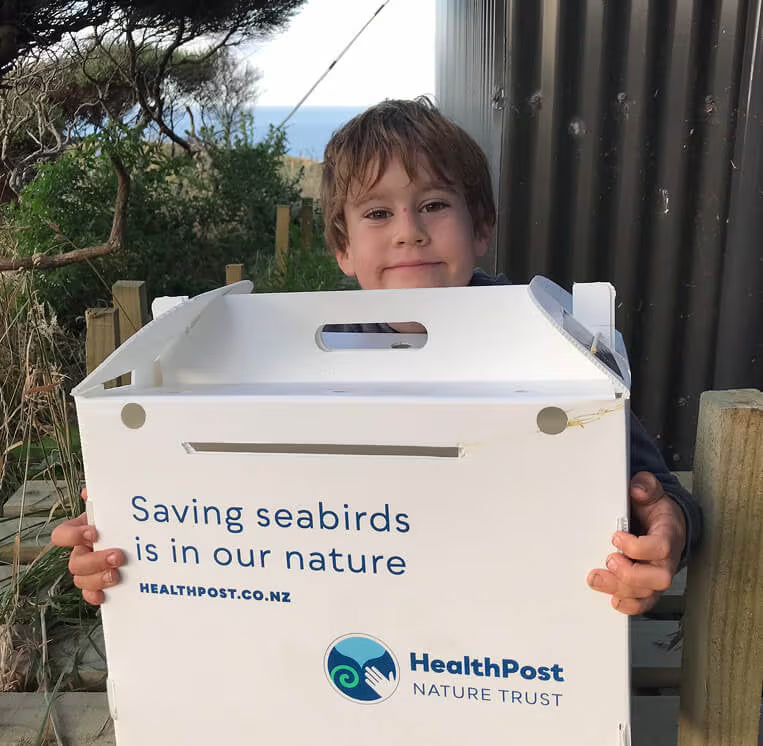 Child holding a box with HealthPost Nature Trust branding and message about seabird conservation.
