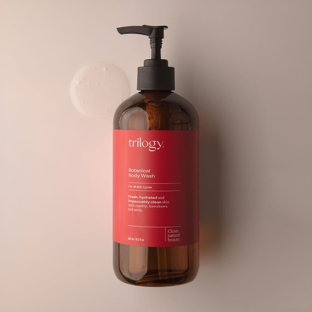 Brown bottle of Trilogy body wash with a red label on a beige background.
