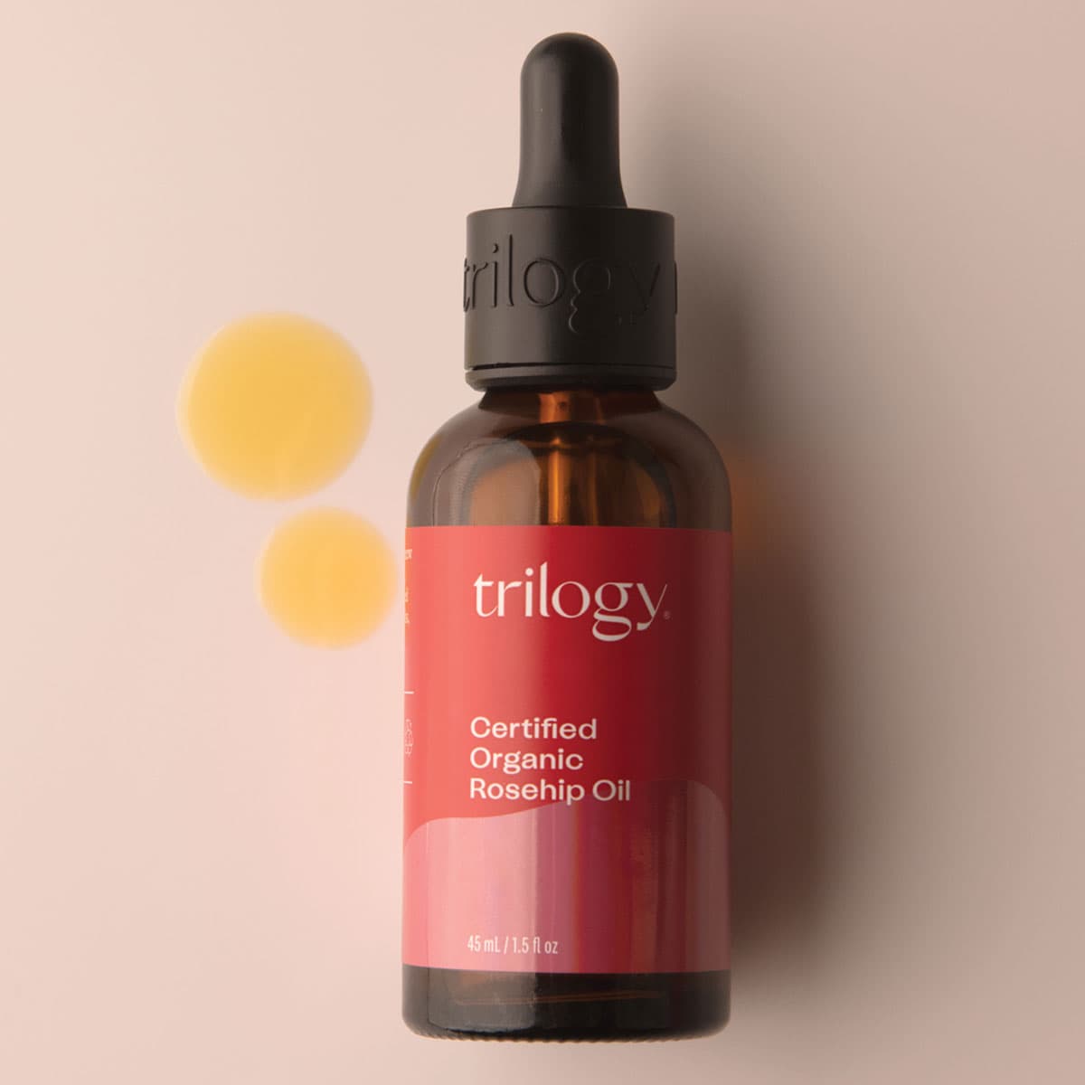 Bottle of Trilogy Certified Organic Rosehip Oil on a beige background.