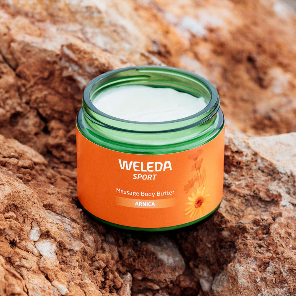Weleda Sport Massage Body Butter jar on a rocky surface.