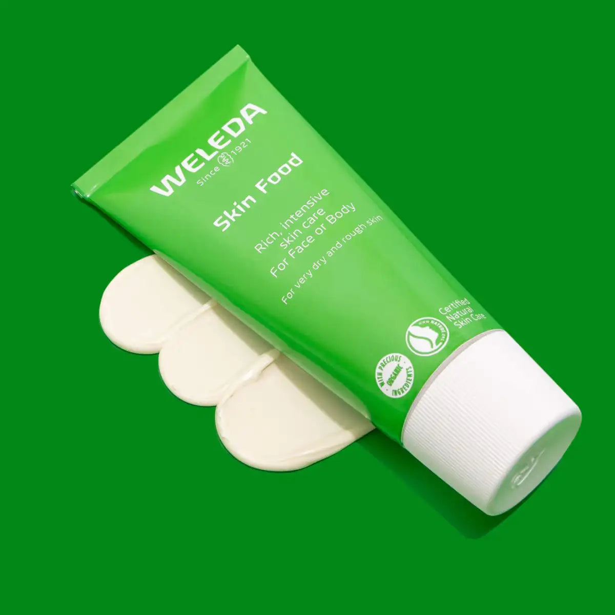 Weleda Skin Food - green tube on a green background with 3 swatches showing smooth & thick texture.