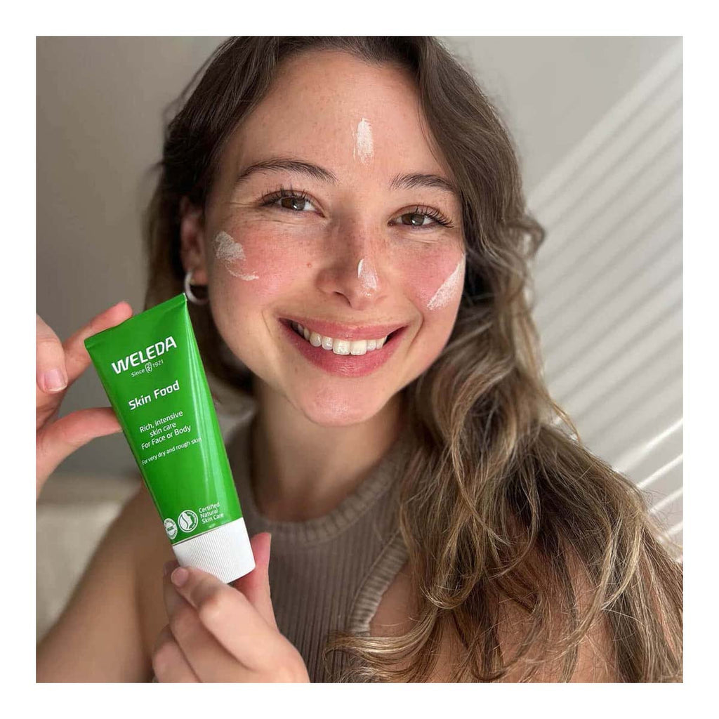 Woman holding a Weleda Skin Food with visible cream on her face