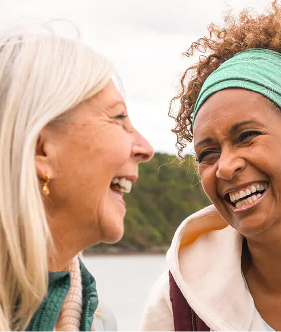 Two women laughing and smiling outdoors with a natural background