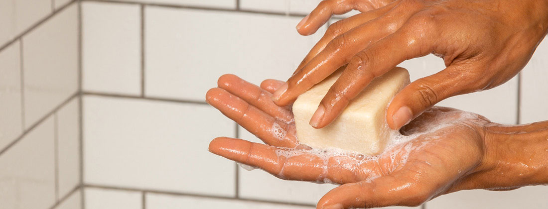 Person holds Ethique beauty bar between hands while in shower