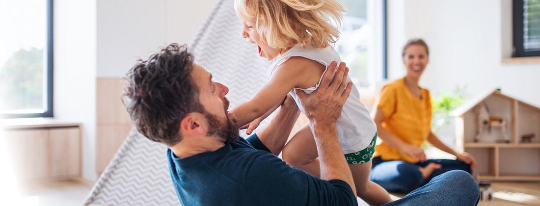 A happy father and child playing rough and tumble, smiling mother in background