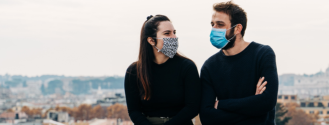 A man and woman sitting outside talking wearing face masks