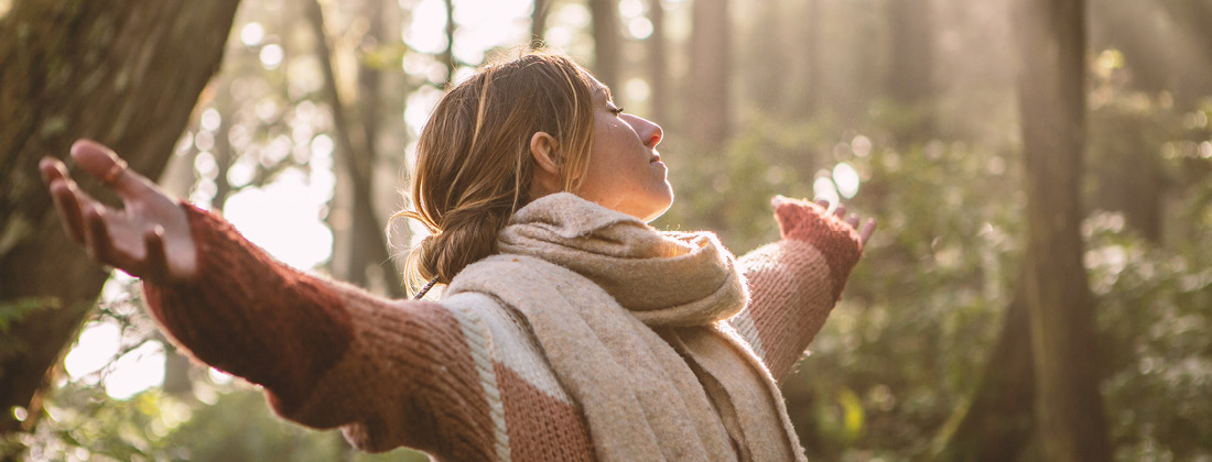 contented woman spreading her arms wide dappled sunlight