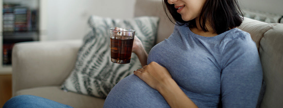 Pregnant woman has hand on stomach and holds cup of tea in other