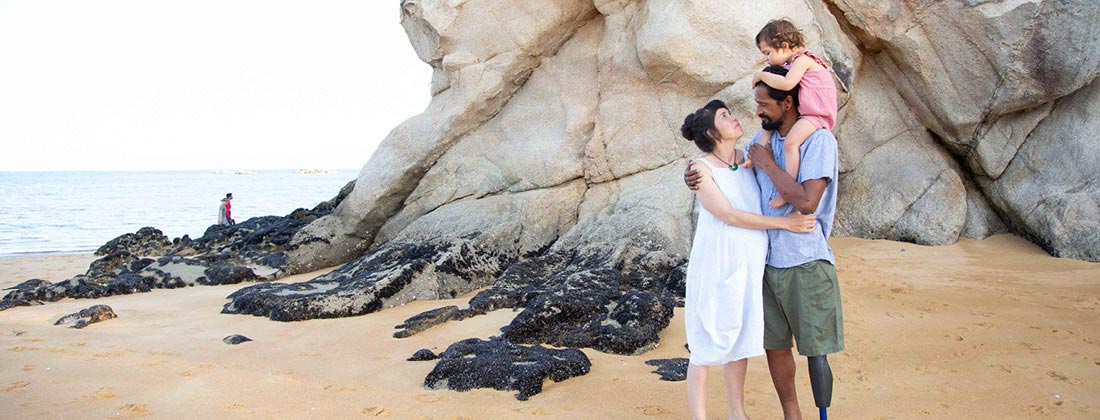 Family of three stand together happily on sand