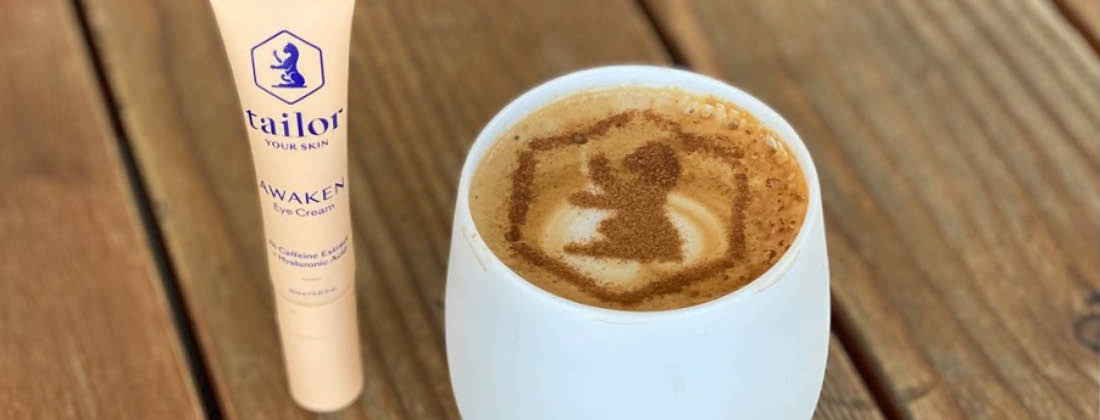 Tailor Skincare Awaken Eye Cream Sits Next To a Cup of Coffee That Has The Tailor Skincare Logo