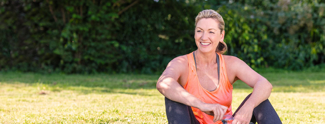 Woman sits happily in workout gear on grass