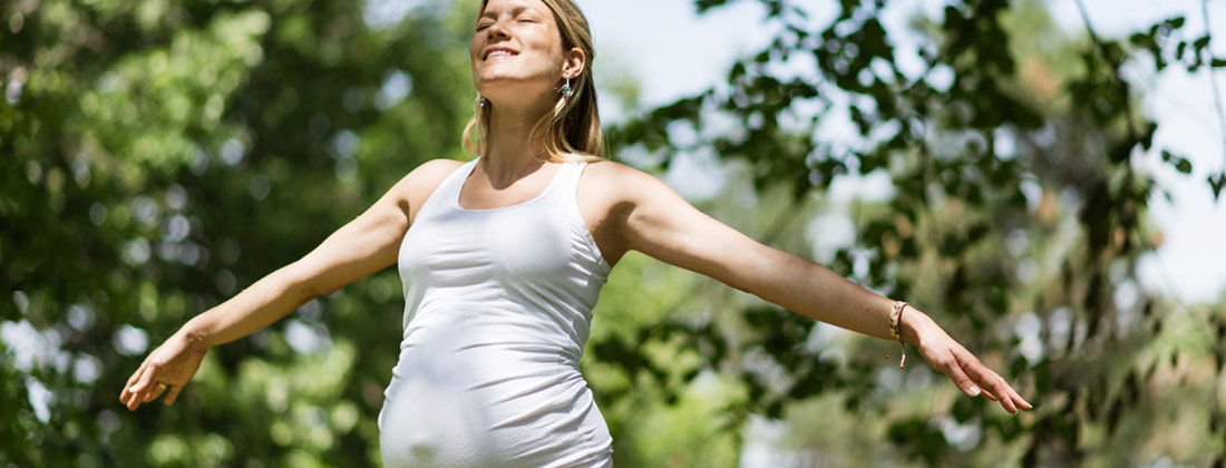 Pregnant woman smiling with arms spread in nature