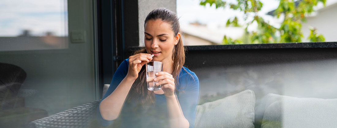 Woman sits surrounded by nature and drinks a beverage