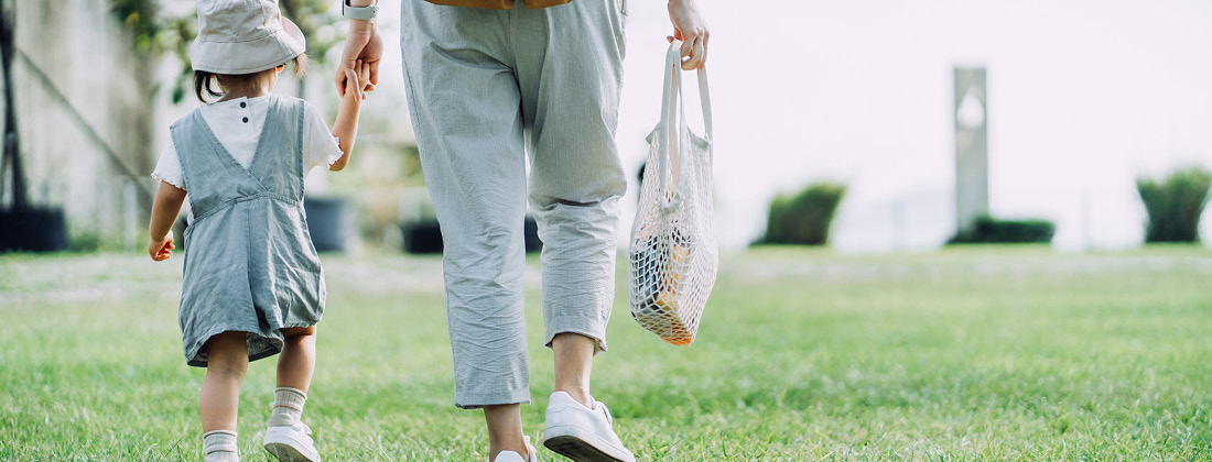 Shot of mother and child walking on grass holding a reusable bag 