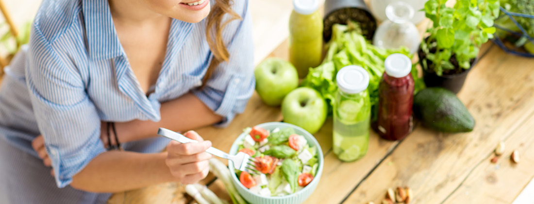 smiling woman eating a fresh salad with fresh produce