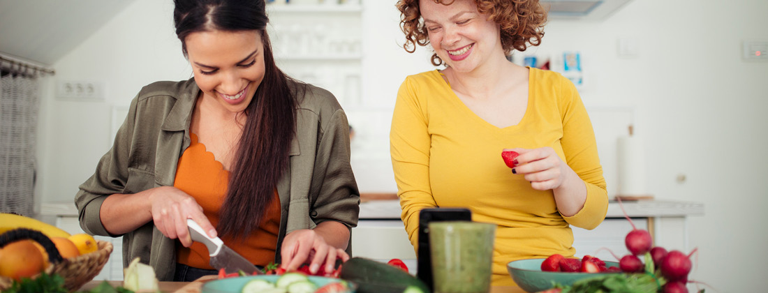 two happy women cutting up strawberries with more produce around