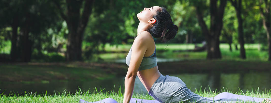 Woman doing yoga in a park - unwind with 10 yoga poses to complement your Tulsi Tea