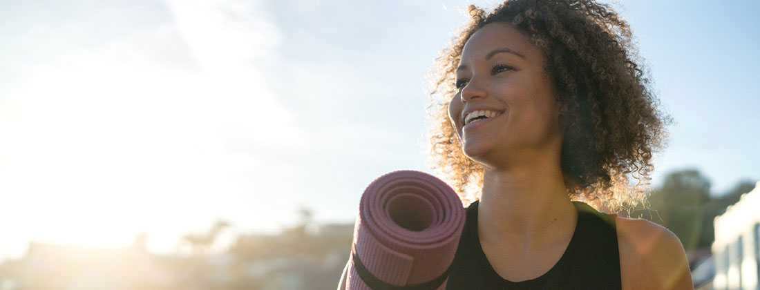 Woman holding yoga mat smiling at sunset