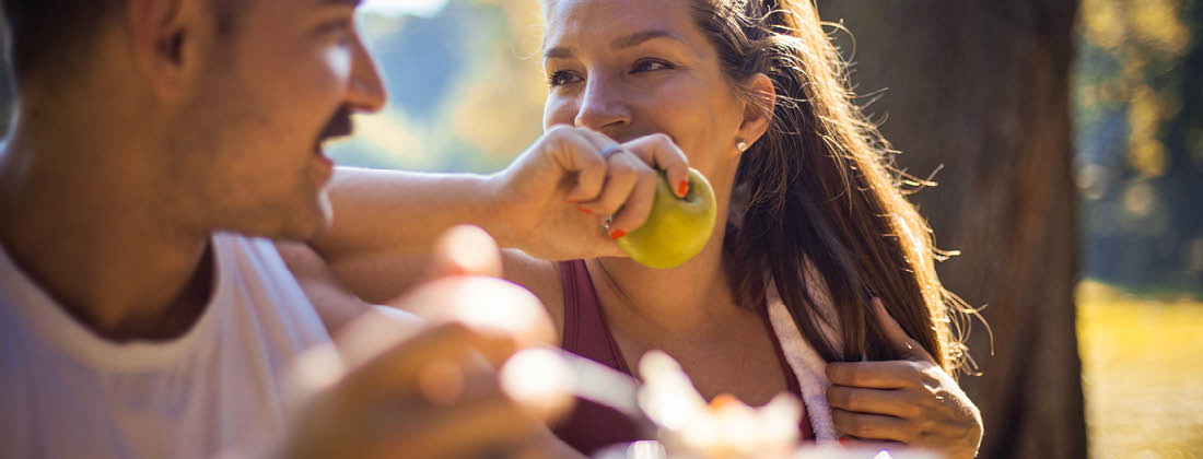 Woman Smiles & Laughs With Friend While Eating A Fruit 