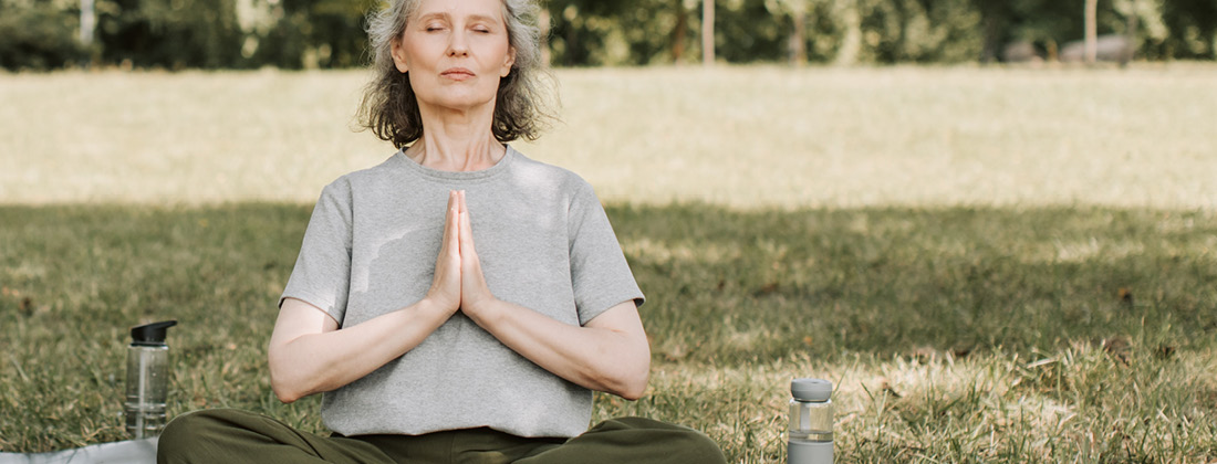 Woman sitting on grass with eyes closed and meditating