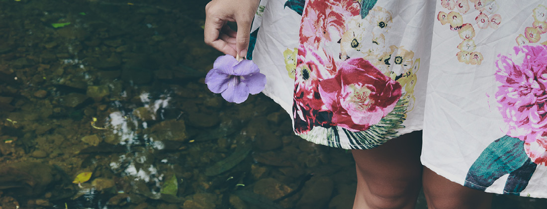 Woman wearing dress and holding flower stands surrounded by nature