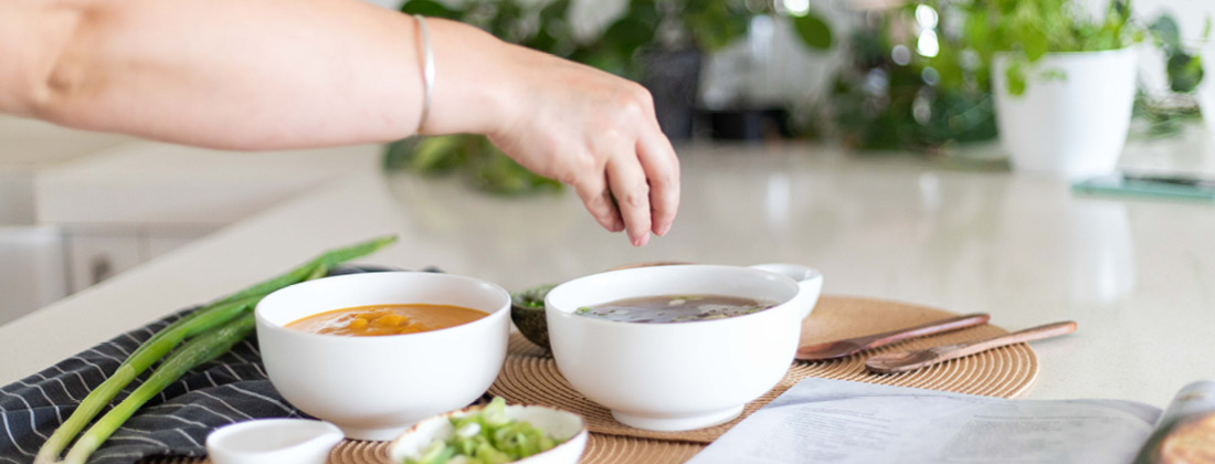 womans hand adding garnish to bowl of nourishing soup